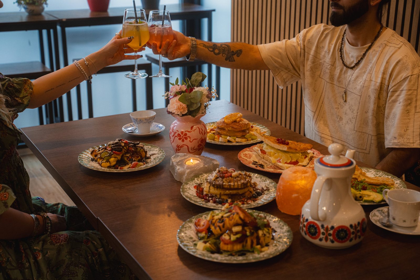 Zwei Gäste stoßen über einem gedeckten Brunchtisch mit hausgemachten Limonaden an